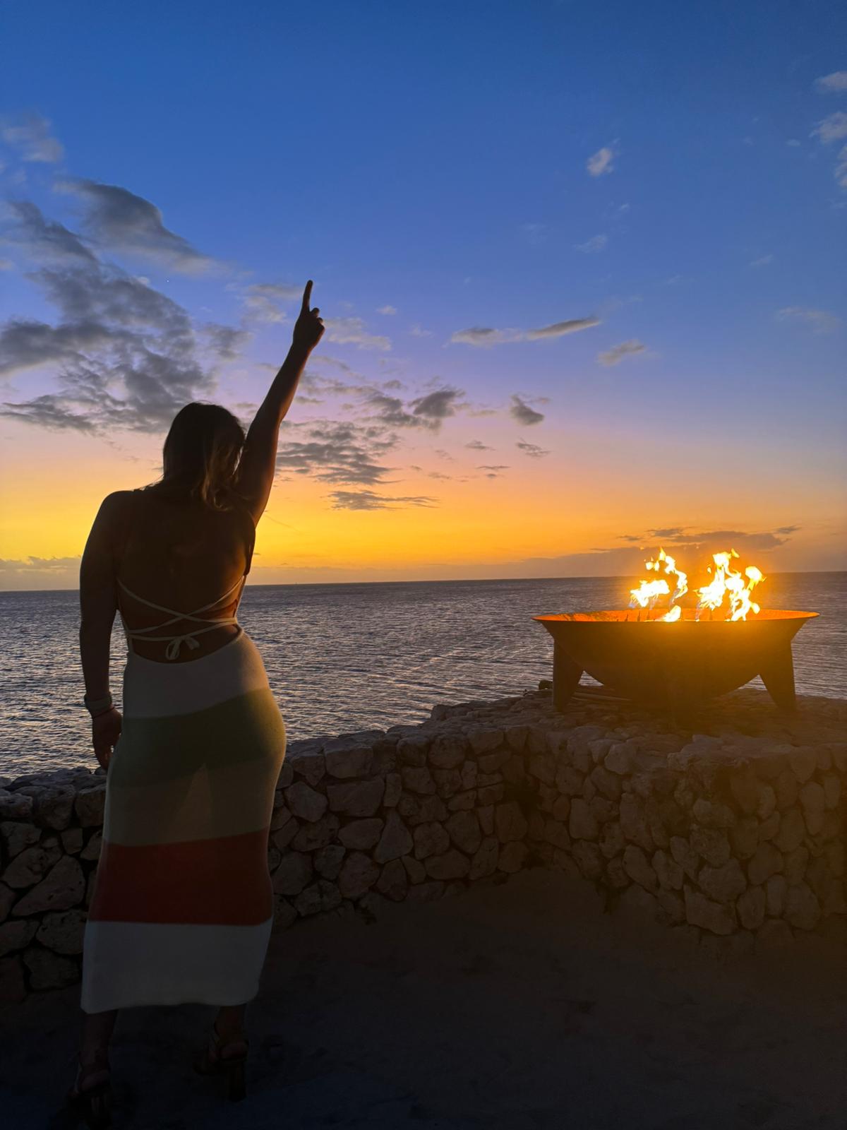 Hayley standing by the ocean at sunset with one arm raised